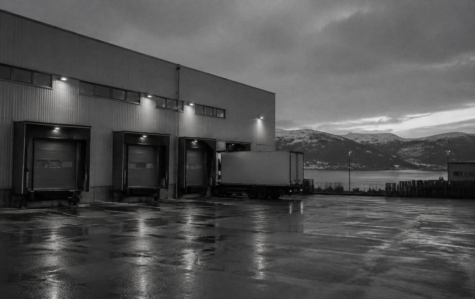 Loading docks of a Norwegian distribution warehouse at dusk with a trailer and a fjord beyond